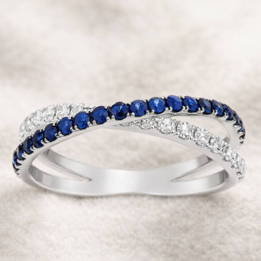 Two intertwined rings, one with blue gemstones and the other with diamonds, on a light background.