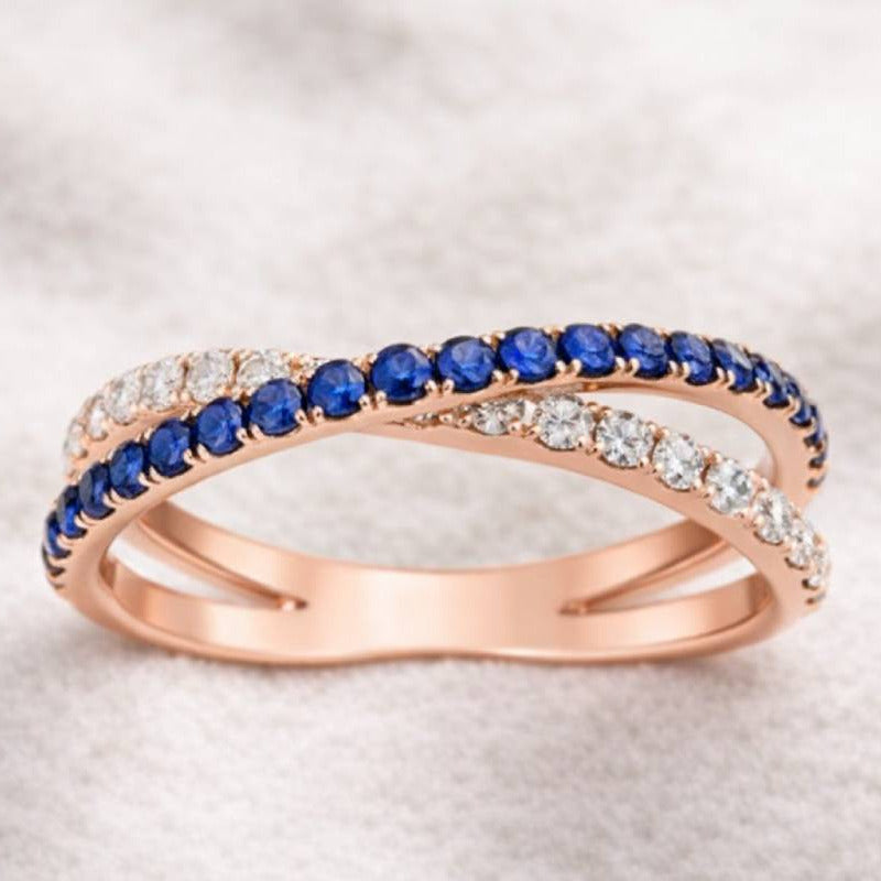 Rose gold ring with blue gemstones and clear stones on a light background