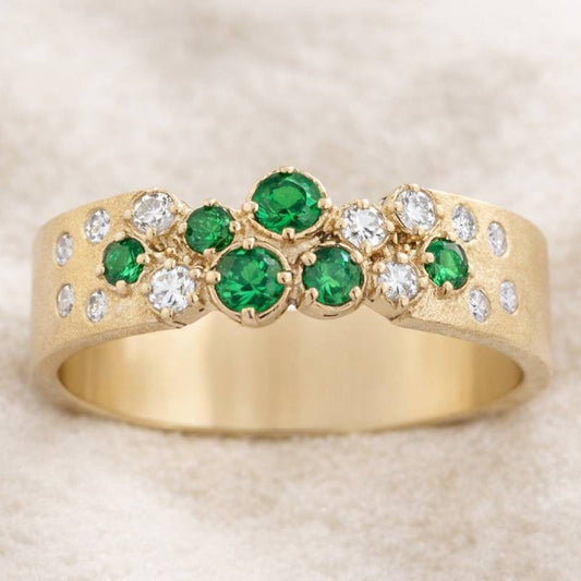 Gold ring with green gemstones and diamonds on a beige background