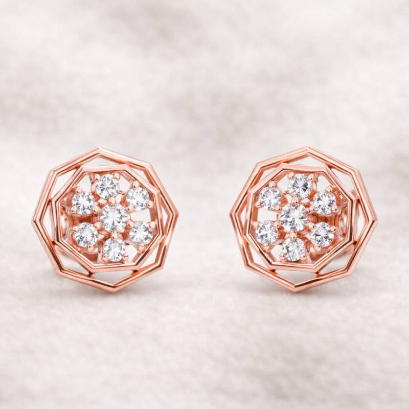Rose gold earrings with diamond-like stones on a soft beige background