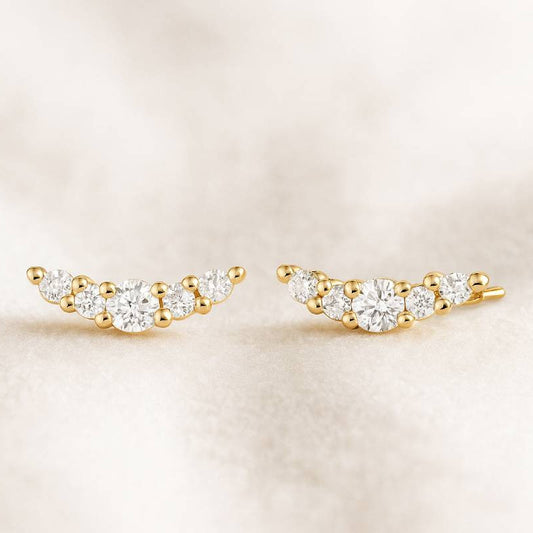 Gold and diamond ear climbers on a beige background