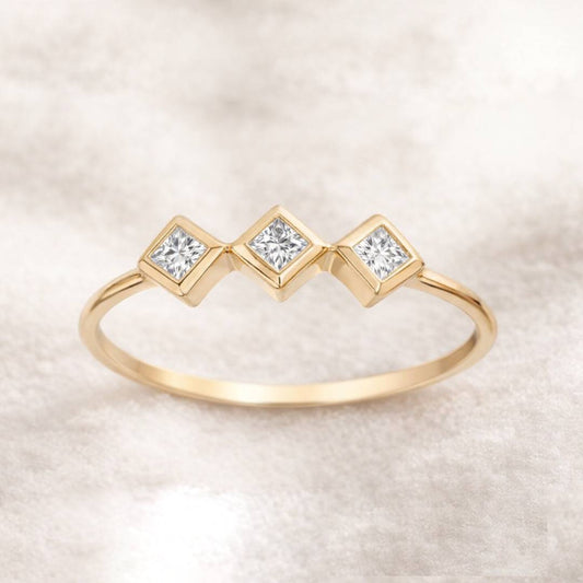 Gold ring with three square-cut diamonds on a light beige background