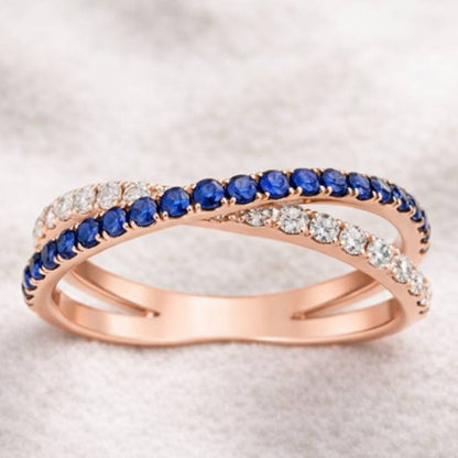 Rose gold ring with blue gemstones and clear stones on a light background