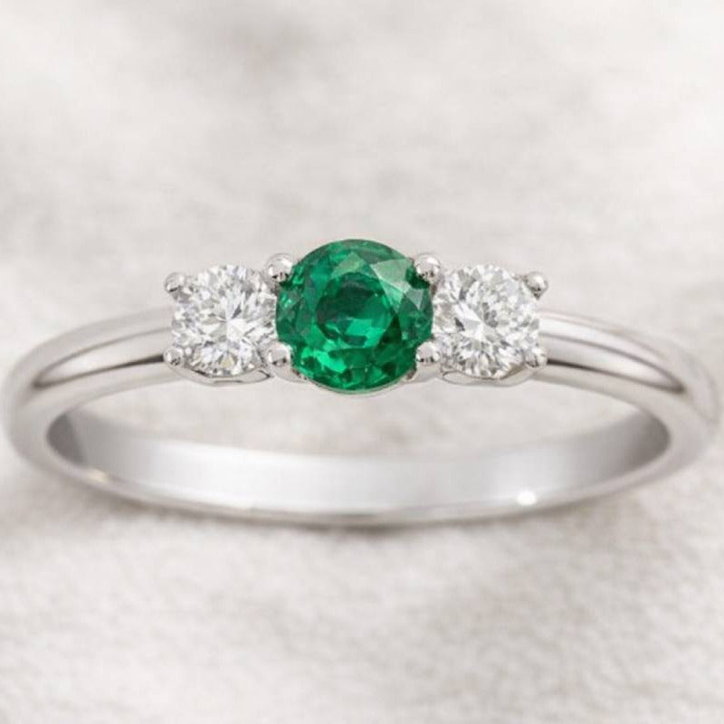  ring with a green gemstone and two smaller diamonds on a light gray background