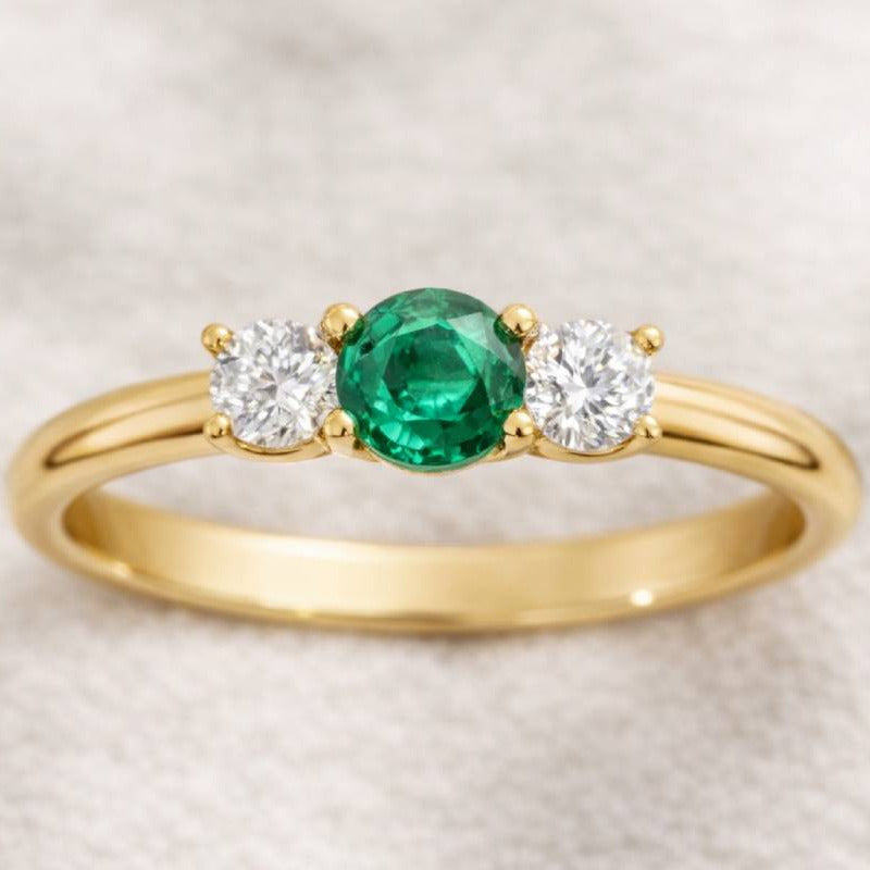 Gold ring with a green gemstone and two white gemstones on a beige background