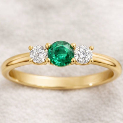 Gold ring with a green gemstone and two white gemstones on a beige background
