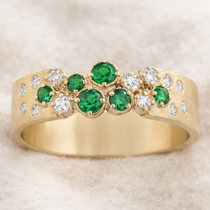 Gold ring with green gemstones and diamonds on a beige background