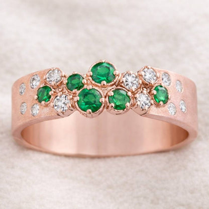 Rose gold ring with green gemstones and clear stones on a light background