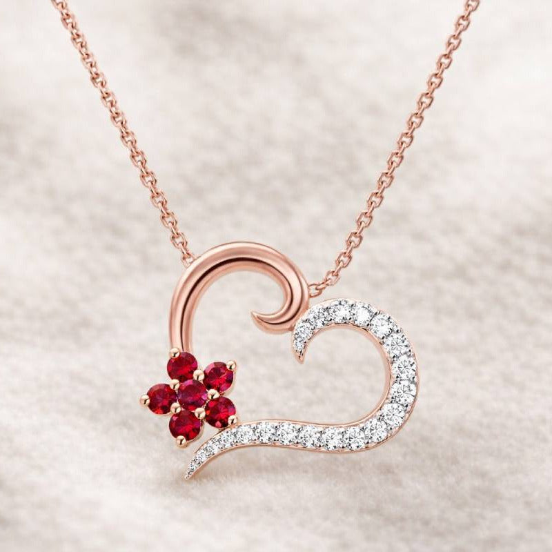 Heart-shaped necklace with red gemstone and diamonds on a light background