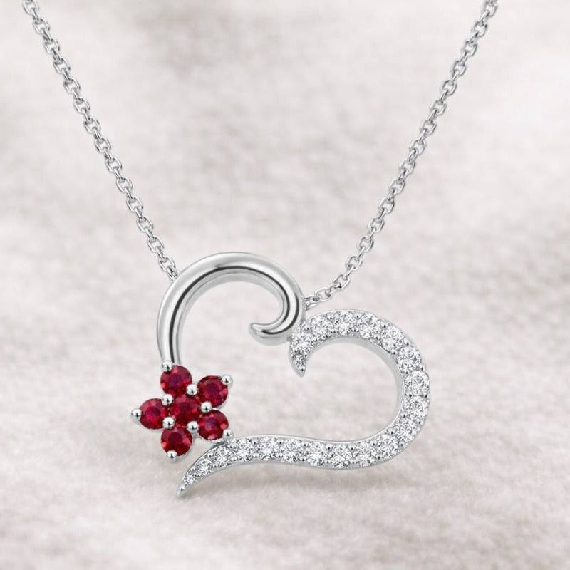 Heart-shaped necklace with a red gemstone on a light gray background
