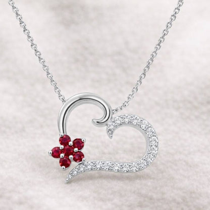 Heart-shaped necklace with a red gemstone on a light gray background
