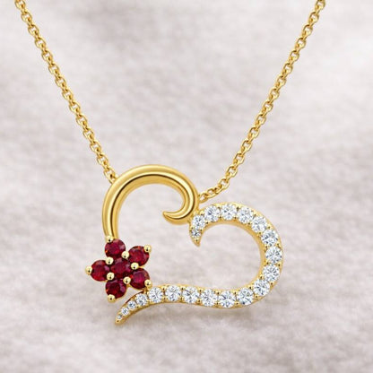 Gold necklace with a heart-shaped pendant featuring red gemstones and diamonds on a light gray background.