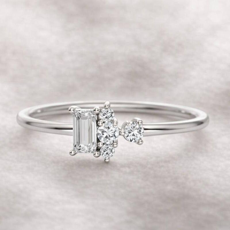 Diamond ring with a central emerald-cut diamond and smaller side stones on a light gray background