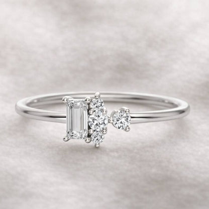 Diamond ring with a central emerald-cut diamond and smaller side stones on a light gray background
