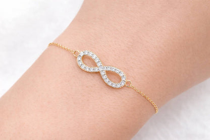 Gold bracelet with an infinity design on a wrist against a white background