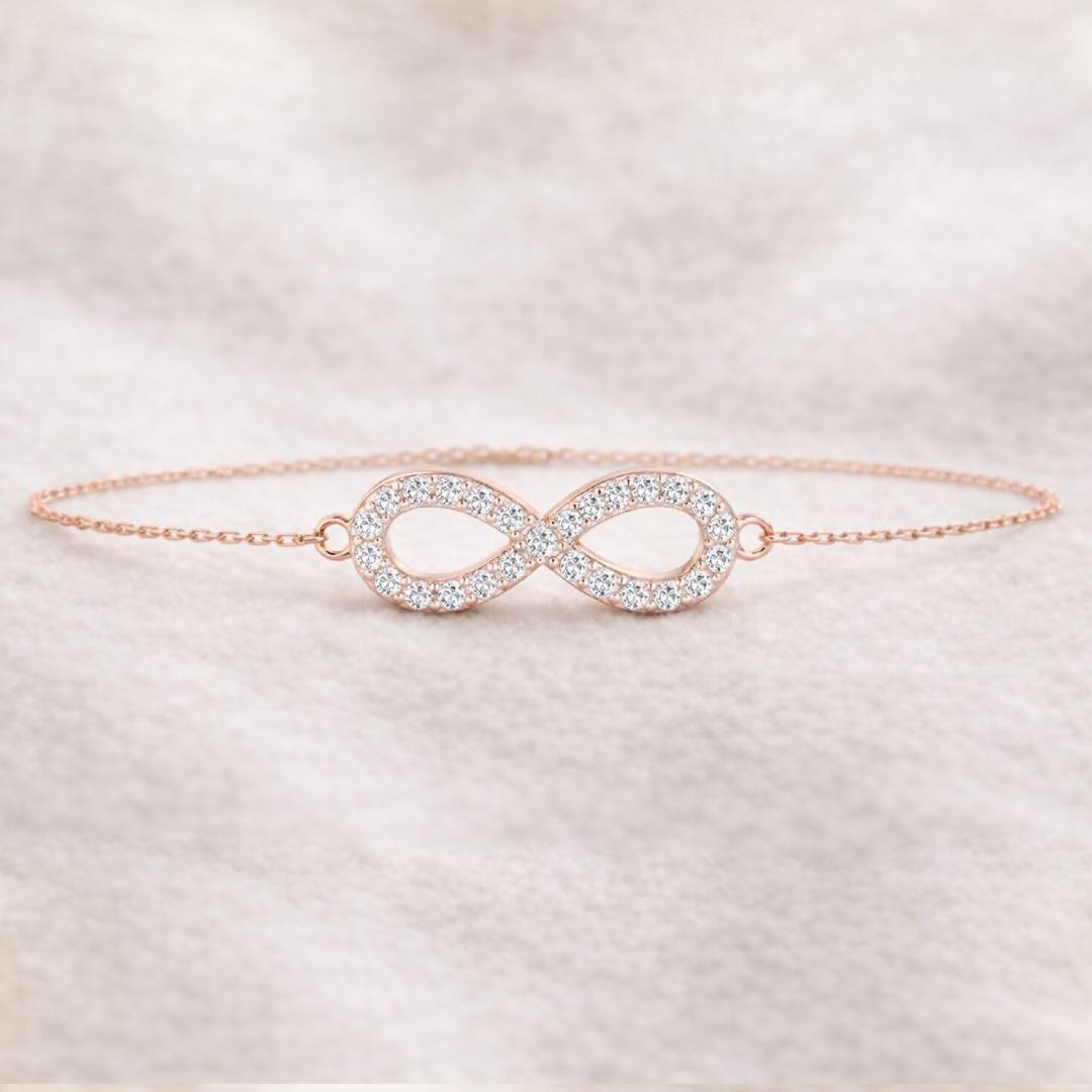 Rose gold infinity bracelet with clear stones on a soft fabric background