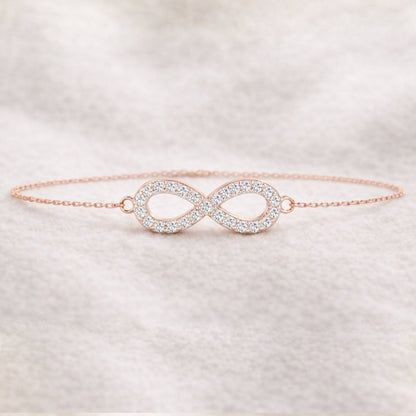 Rose gold infinity bracelet with clear stones on a soft fabric background