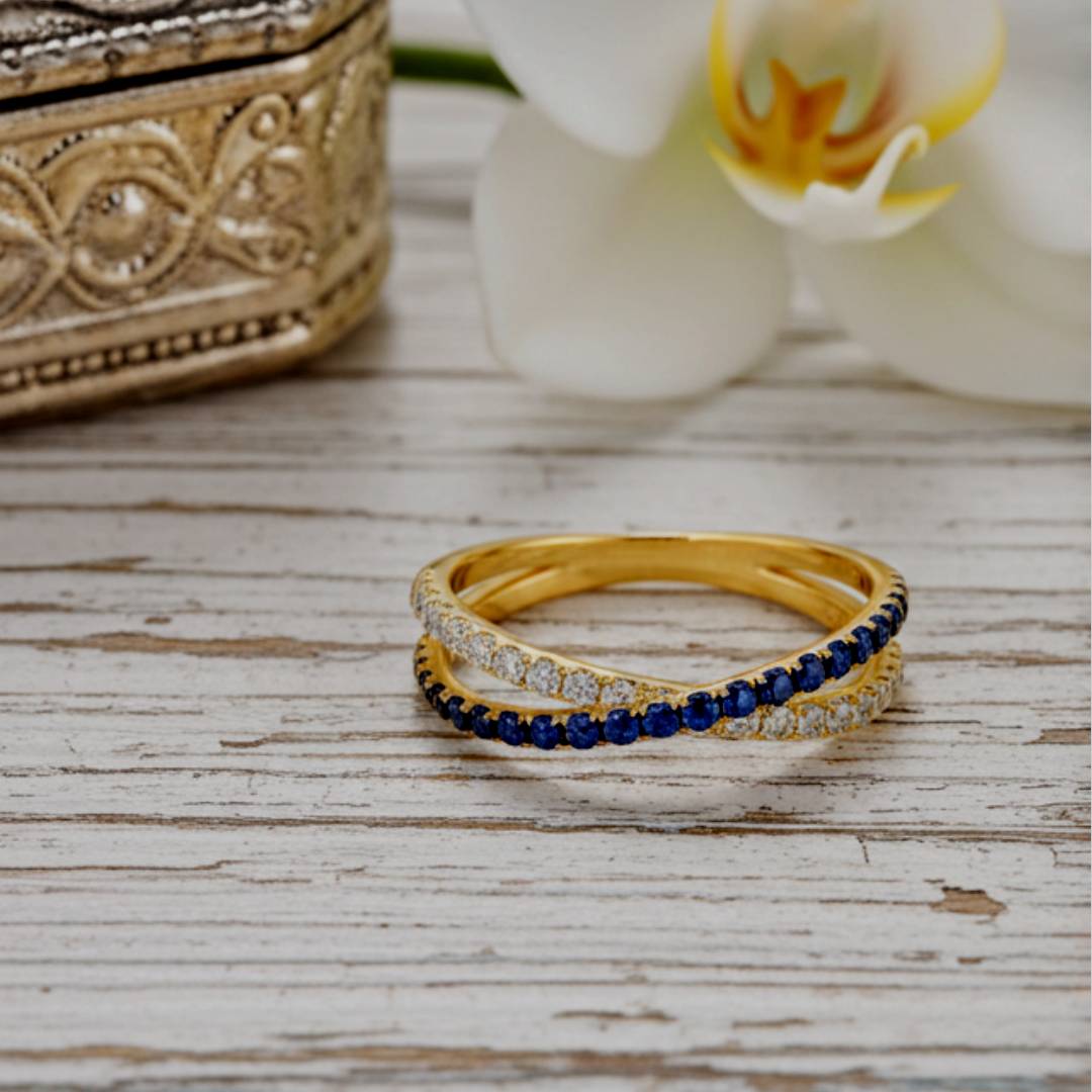Gold ring with blue gemstones on a wooden surface with a decorative box and white orchid in the background.
