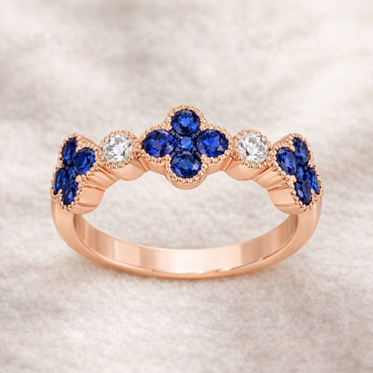 Rose gold ring with blue gemstones and clear stones on a textured beige background