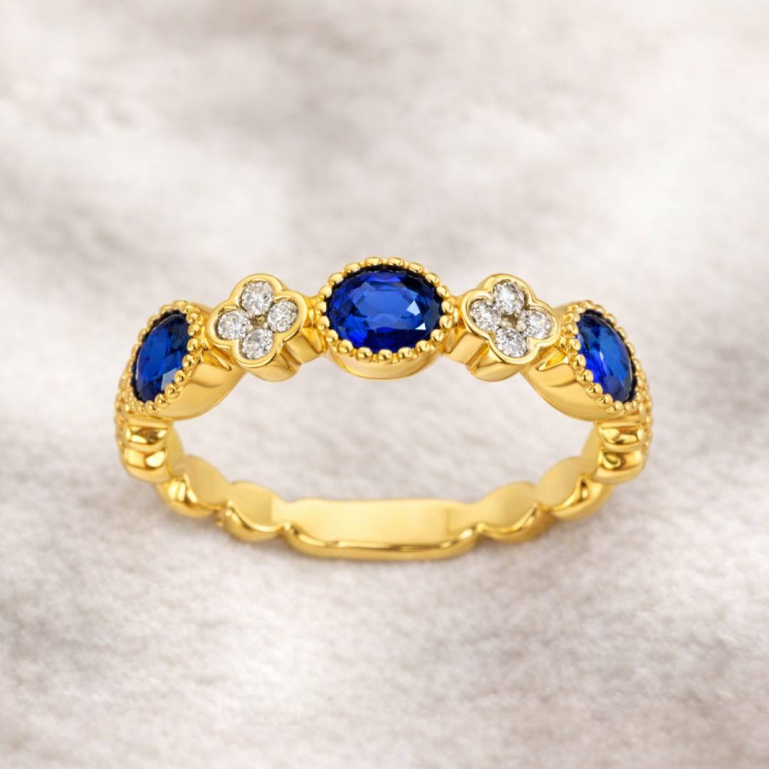 Gold ring with blue gemstones and diamond accents on a textured beige background