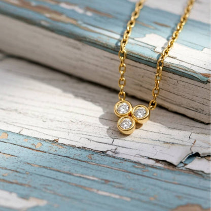 Gold necklace with three circular pendants on a rustic wooden surface