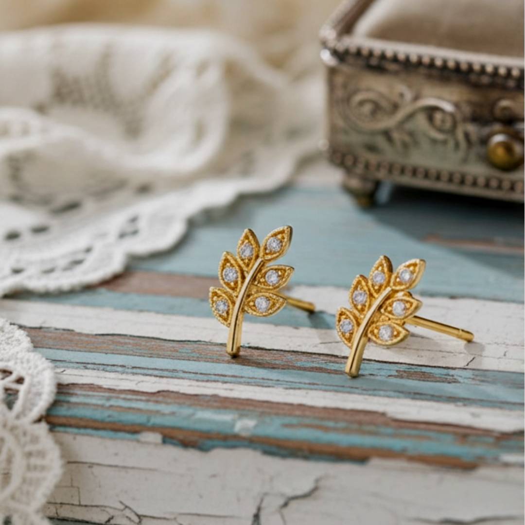 Gold leaf-shaped earrings with clear stones on a textured surface.