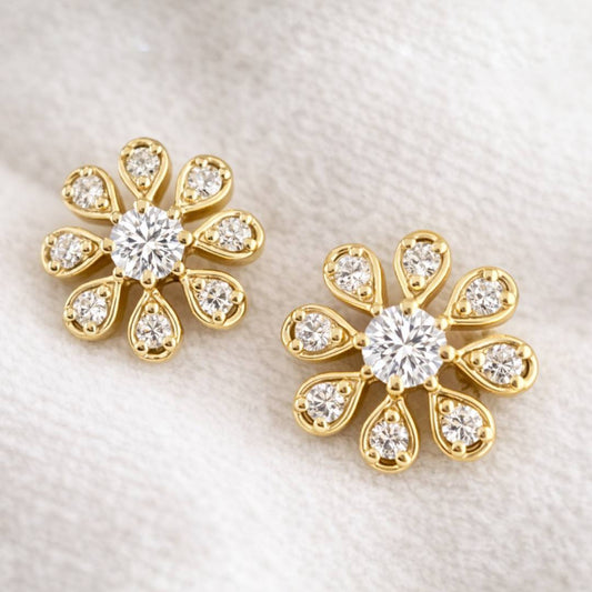 Pair of gold flower-shaped earrings with clear gemstones on a light fabric background