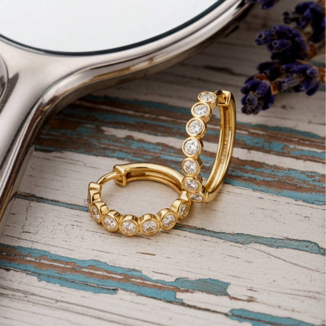 Gold hoop earrings with clear stones on a textured wooden surface.