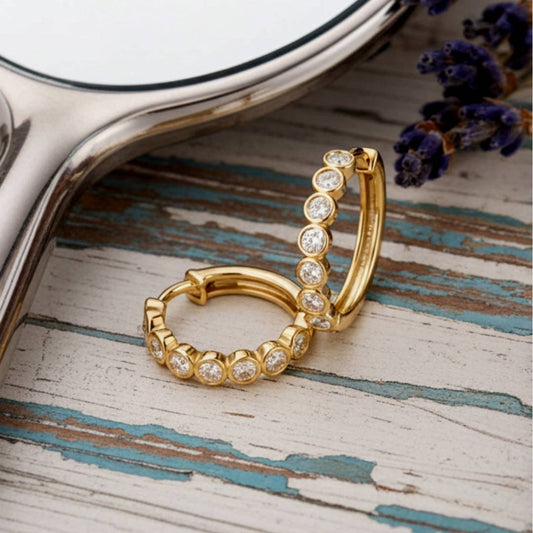 Gold hoop earrings with clear stones on a textured wooden surface.