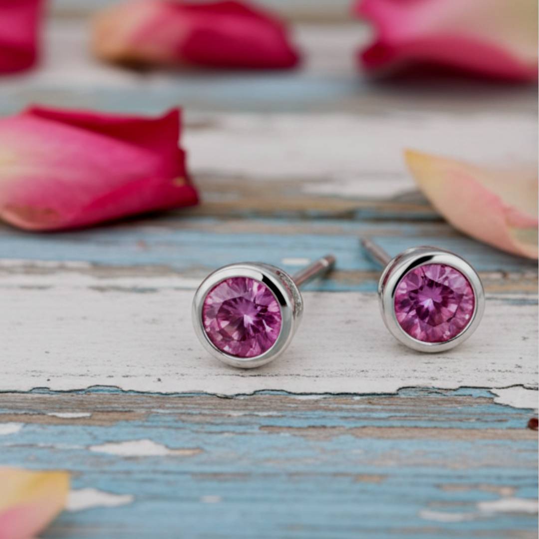 Pink stud earrings on a wooden surface with pink petals in the background