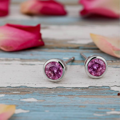 Pink stud earrings on a wooden surface with pink petals in the background