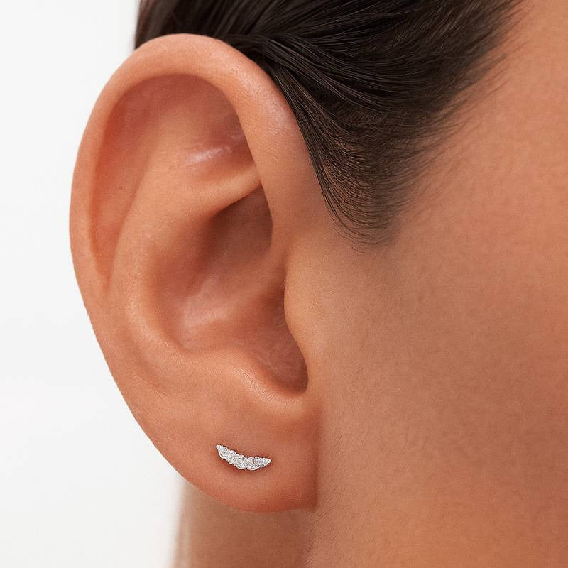 Close-up of an ear wearing a diamond earring on a white background