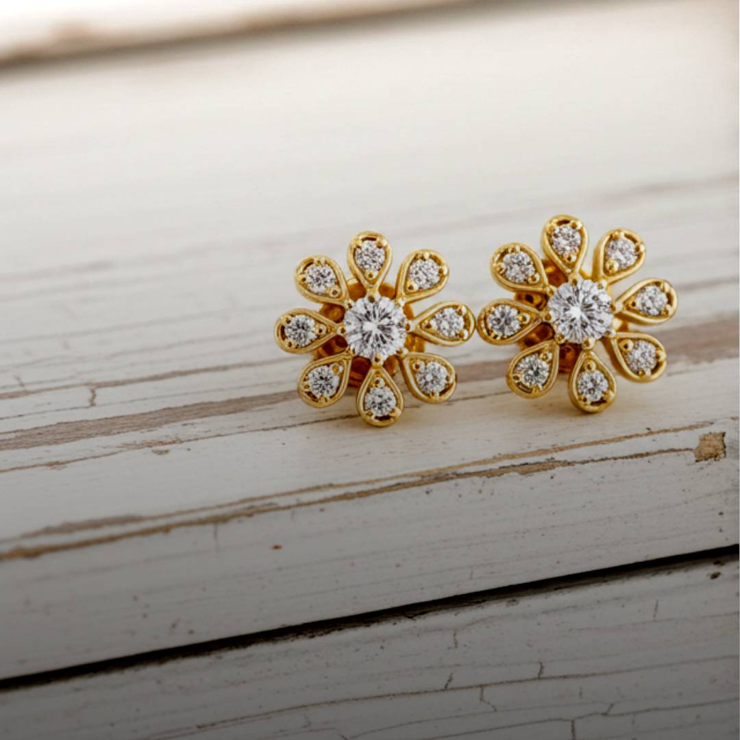 Gold flower-shaped earrings with clear stones on a wooden surface