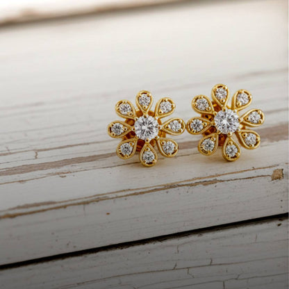 Gold flower-shaped earrings with clear stones on a wooden surface
