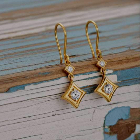 Gold earrings with diamond-like stones on a wooden surface