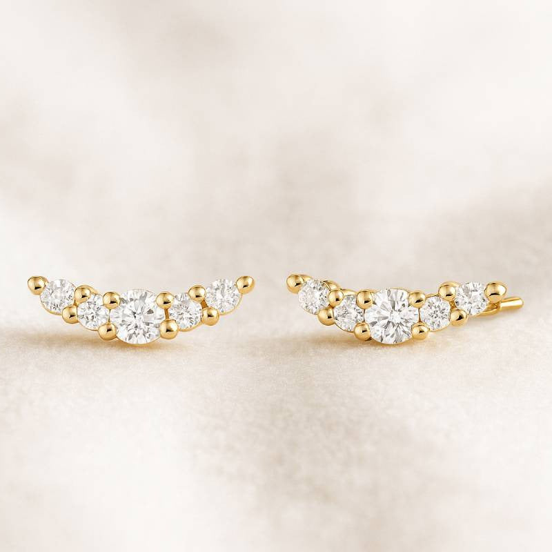 Gold and diamond ear climbers on a beige background