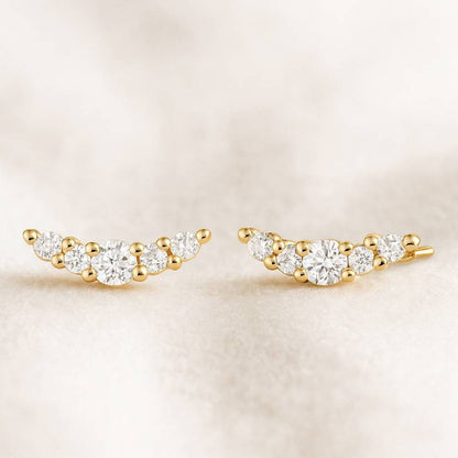 Gold and diamond ear climbers on a beige background