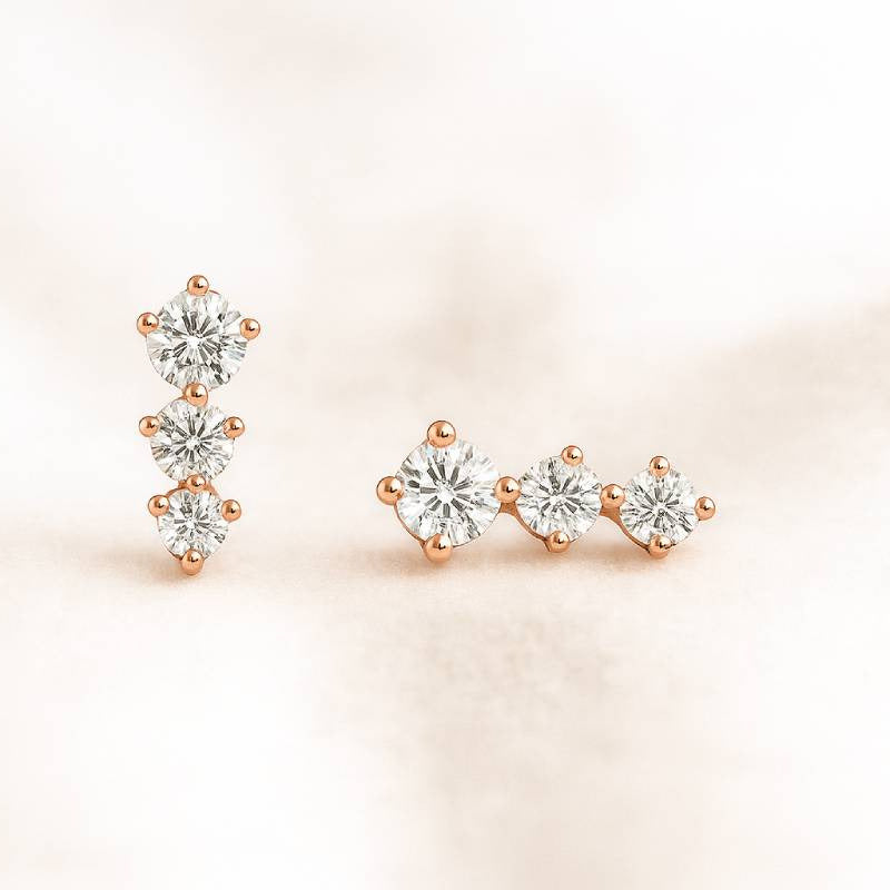 Pair of rose gold and clear gemstone earrings on a soft pink background