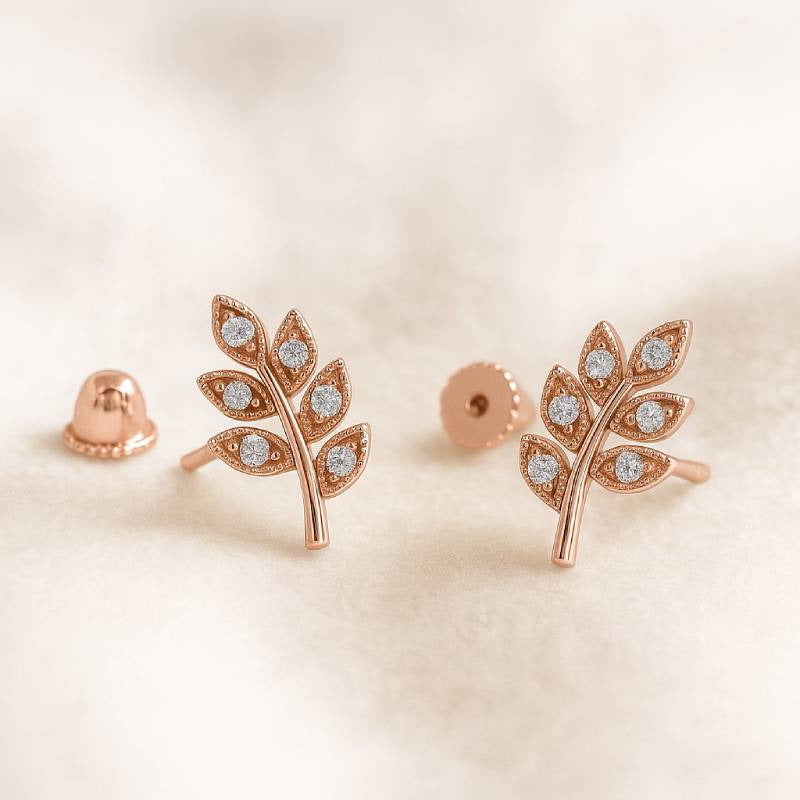Rose gold leaf-shaped earrings with gemstones on a beige background