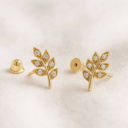 Gold leaf-shaped earrings with embedded stones on a light background