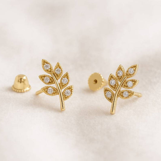 Gold leaf-shaped earrings with embedded stones on a light background