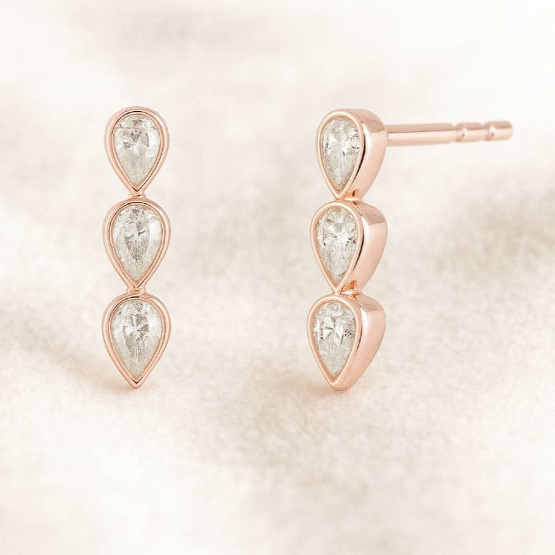 Rose gold earrings with three teardrop-shaped gemstones on a light pink background