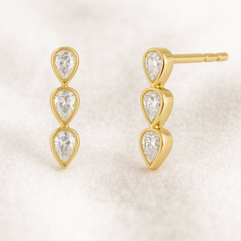 Gold earrings with three teardrop-shaped gemstones on a light background
