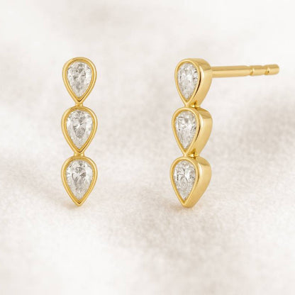 Gold earrings with three teardrop-shaped gemstones on a light background