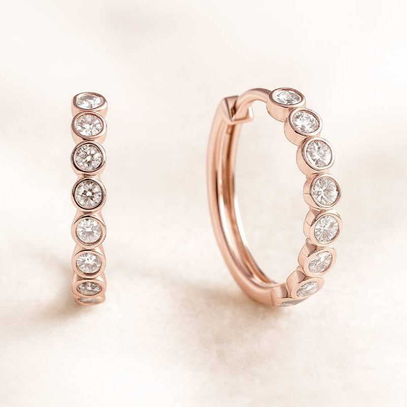Rose gold hoop earrings with embedded diamonds on a light pink background