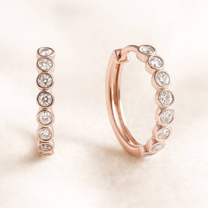 Rose gold hoop earrings with embedded diamonds on a light pink background