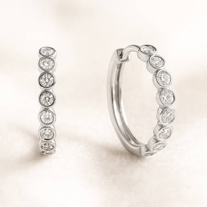 Pair of hoop earrings with clear gemstones on a light beige background