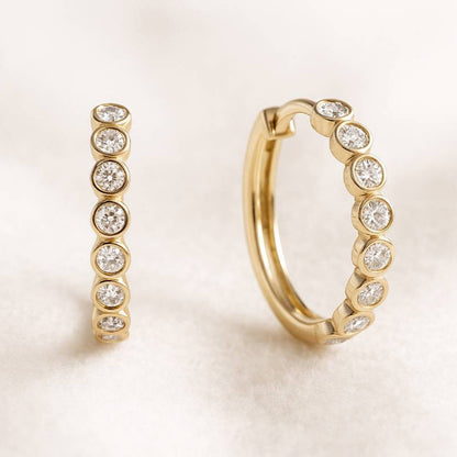 Gold hoop earrings with embedded diamonds on a light background