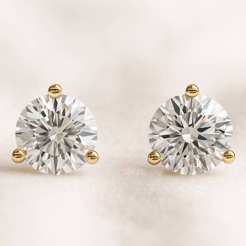 Pair of diamond stud earrings with gold posts on a light beige background
