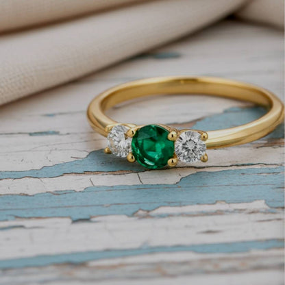 Gold ring with a green gemstone and two diamonds on a textured surface
